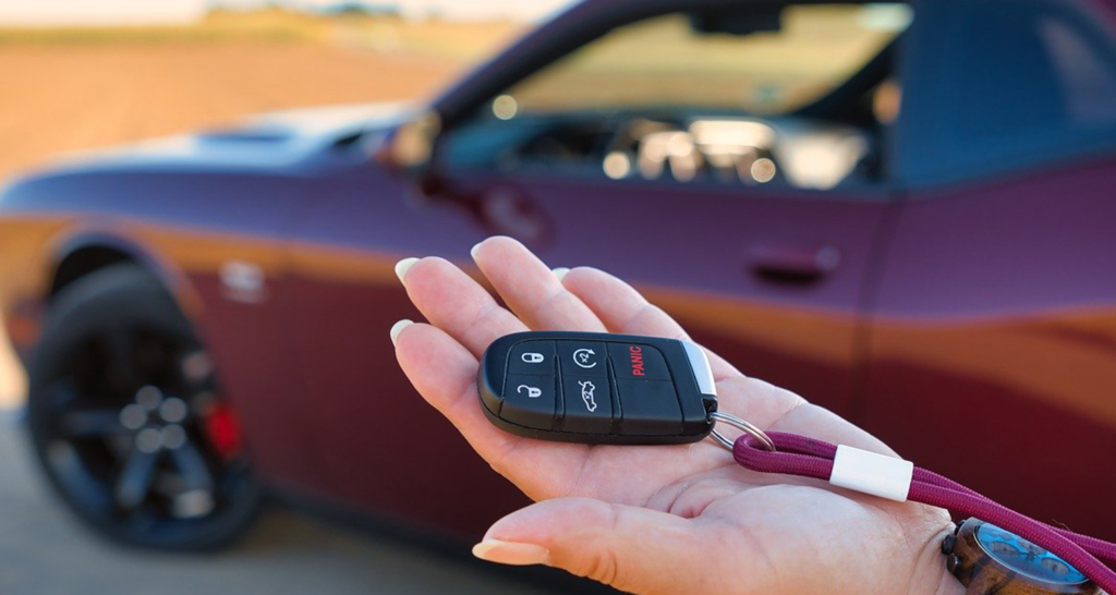 hand holding key and red car in the background